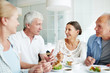 © pressmaster - Friendly senior people gathered by table having talk by dessert with tea