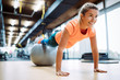 © NDABCREATIVITY - Young attractive woman doing push ups using ball