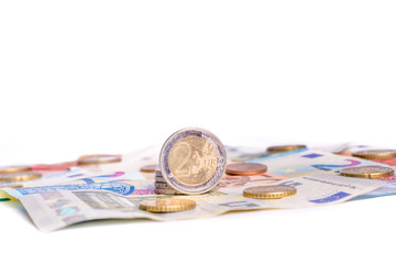 Two Euro coin on Euro bank notes and other coins close up on white background