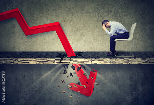 Cuadros en Lienzo Depressed business man looking down at the falling red arrow going through a concrete floor