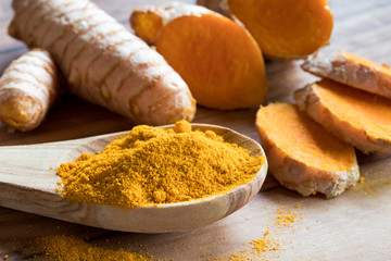 Turmeric powder on a wooden spoon, with turmeric root in the background