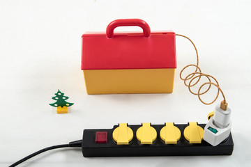 A red and yellow toy house depicting an apartment building. Household extender. Wires brought to the house. The concept of electricity and electrical installation works.