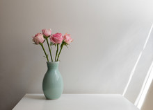 Pink Roses In Green Vase On White Table Against Neutral Background With Window Light