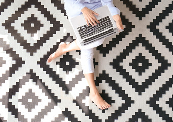 Poster - Young woman using laptop while sitting on carpet