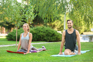 Sticker - Young man and woman doing exercises on yoga mats in park