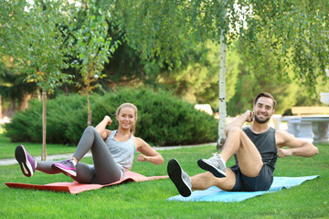 Poster - Young man and woman doing exercises on yoga mats in park