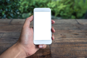 Mockup image of a man's hand holding and using white smart phone with blank screen on wooden table and green nature background