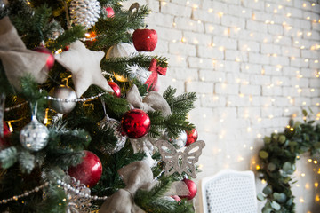 Christmas tree with red balls and self-made stars on the background of a brick wall with garlands and a Christmas wreath