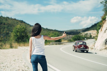 Beautiful Young Female Hitchhiking At The Country Road. Hitchhiking Tourism Concept. Travel Hitchhiker Woman Walking On Road During Holiday Travel