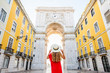 Young woman tourist in red dress standing back in front of the famous triumphal arch in Lisbon city center in Portugal
