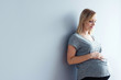 © Karniewska - Young pregnant woman standing against gray wall, eyes closed.