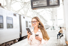 Portrait Of A Young Woman Using Smart Phone At The Railway Station With Information Board On The Background