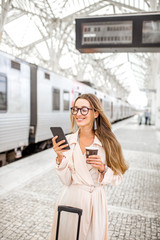 Wall Mural - Portrait of a young woman using smart phone at the railway station with information board on the background