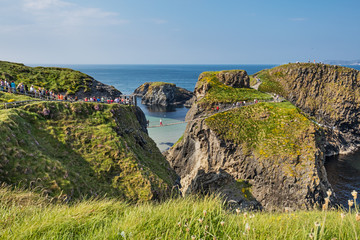 Wall Mural - Thousands of tourists visiting Carrick-a-Rede Rope Bridge in County Antrim of Northern Ireland, hanging 30m above rocks and spanning 20m, linking mainland with the tiny island of Carrickarede