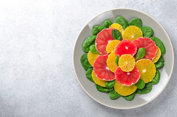 Wall Mural - Salad made of orange and grapefruit slices and spinach leaves on a gray plate on light stone background. Top view, horizontal image