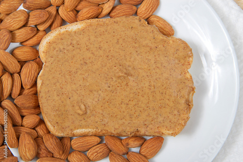 Valokuva Almond butter spread on bread on a white plate surrounded by whole raw almonds