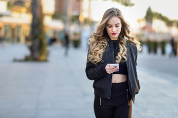 Wall Mural - Blonde woman texting with her smartphone in urban background