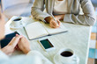 © Seventyfour - Closeup of two unrecognizable businesswomen working in cafe writing notes in planner and drinking coffee