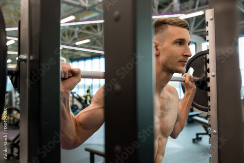 Plakat Portret przystojny młody sportowiec wpisuje ciężkiego barbell w gym z nagą klatką piersiową, strzał od behind ważenia stojaka