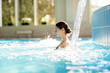 Leinwandbild Motiv Serene girl enjoying stream of waterfall and its gentle splashes in swimming-pool at spa resort