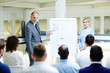 © pressmaster - Confident mature expert by whiteboard making presentation of data and explaining it to learners