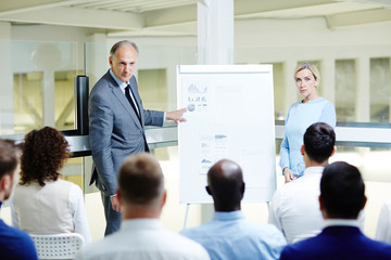 Canvas Print - Confident mature expert by whiteboard making presentation of data and explaining it to learners