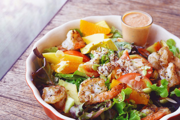 Fresh fruit salad with grilled shrimp and salad dressing served on red bowl.