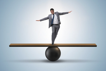 businessman trying to balance on ball and seesaw