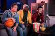 © Yakobchuk Olena - So exciting. Three young interested guys are sitting on sofa and expressing exhilaration while watching sport game with opened mouthes. Friends are eating popcorn and drinking beer