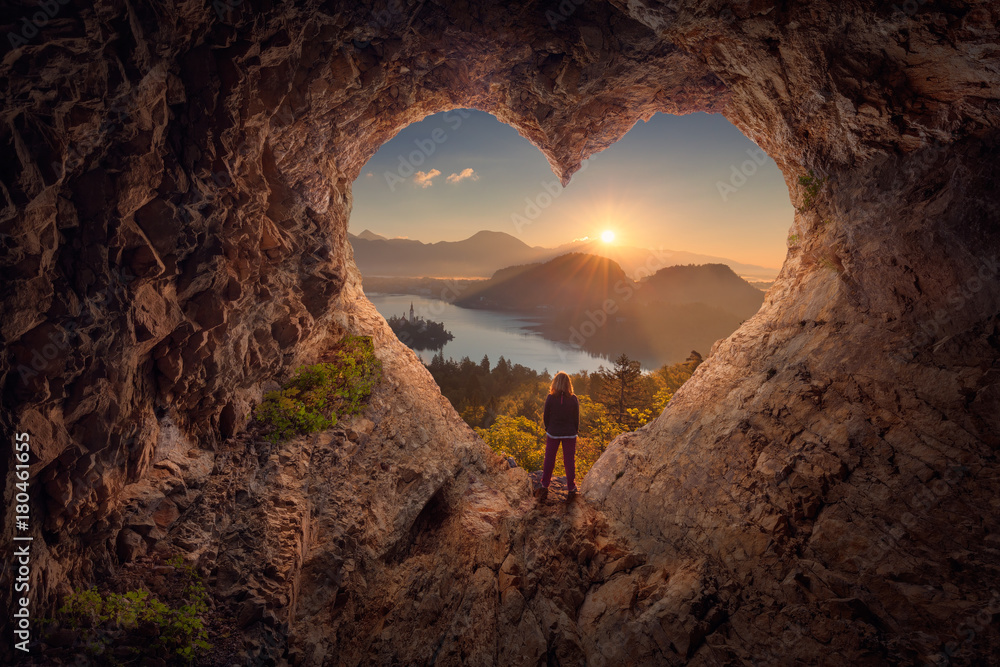 Young woman in heart shape cave towards the idyllic unrise - obrazy, fototapety, plakaty 