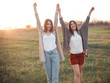 Two young women smiling and raising hands up on sunset background
