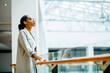 © Iryna - young african business woman in glasses dressed in gray suit holding on handrail when looking up and thinking indoor at modern business center. People lifestyle concept.
