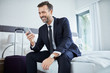 © baranq - Cheerful businessman using phone sitting in hotel room on business trip