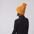 Woman wearing mustard knit beanie hat with big pom pom and black turtleneck isolated on grey background. Copy space