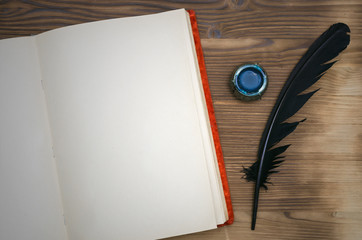 Open vintage book with blank paper page with copy space, black feather pen and inkwell on table background. Education background. Writer desk table.