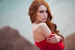 portrait of a beautiful young girl with red hair in a red tight dress near the lake shore