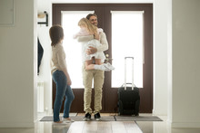 Happy Father Arrived Home Returning After Business Trip With Baggage, Daddy Missed Little Daughter Holding In Arms Hugging Girl While Wife Standing In Hall, Family Reunion, Welcome Back Dad Concept
