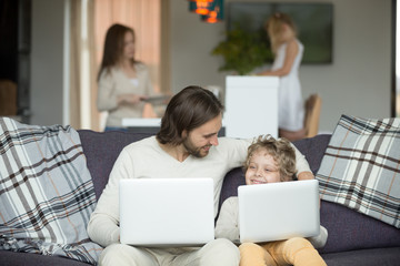 Sticker - Happy father and son embracing using laptops together at home, smiling dad and boy bonding holding computers sitting on sofa, kid imitating copying daddy with pc on couch, like father like son