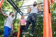 Low-angle view of a strong young man doing chin-up repetitions for the upper-body during calisthenics workout, with his friends in a modern outdoor fitness park