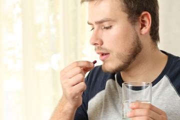 Serious man taking a pill at home