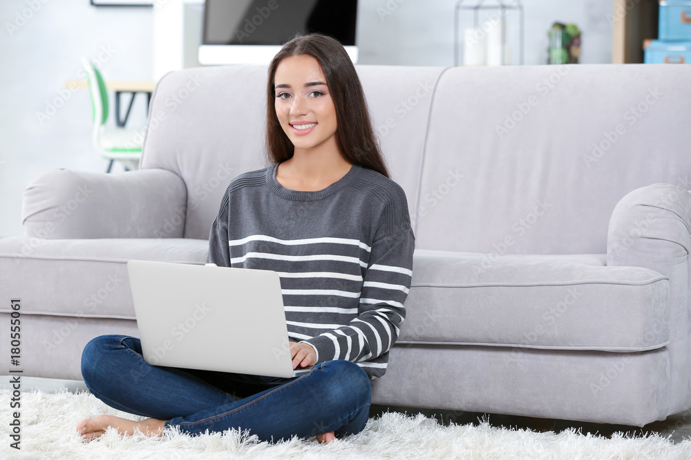 Young woman with modern laptop on carpet at home