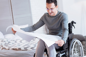 So cute. Positive invalid man bowing head and keeping smile on his face while being on wheelchair