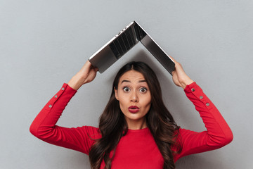 Sticker - Shocked brunette woman in red blouse holding laptop computer overhead