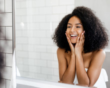 Happy Woman Admiring Her Skin In Front Of The Bathroom Mirror, Touching Face With Hands