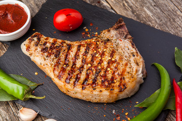 Grilled pork steak on the bone with seasonings and grilled tomatoes on a black background. Top view