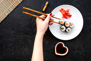 Wall Mural - Hand takes sushi roll with salmon and avocado with chopstick. Black background top view