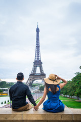 Young couple of tourists sitting in front of Eiffel tower in Paris, vertical view