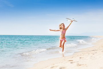 Wall Mural - Little girl running on the coast with toy plane