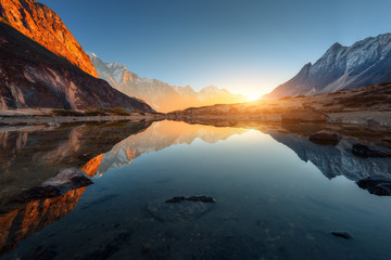 Wall Mural - Wonderful landscape with high rocks with illuminated peaks, stones in mountain lake, reflection, blue sky and yellow sunlight in sunrise. Nepal. Amazing scene with Himalayan mountains. Himalayas