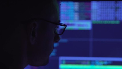 Male hacker working on a computer in a dark office room.